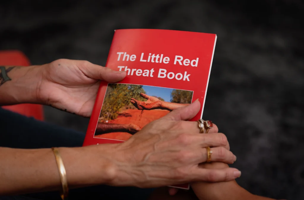 A lady's hands passing over 'the little red threat book' as a sign to spread awareness around mental health.