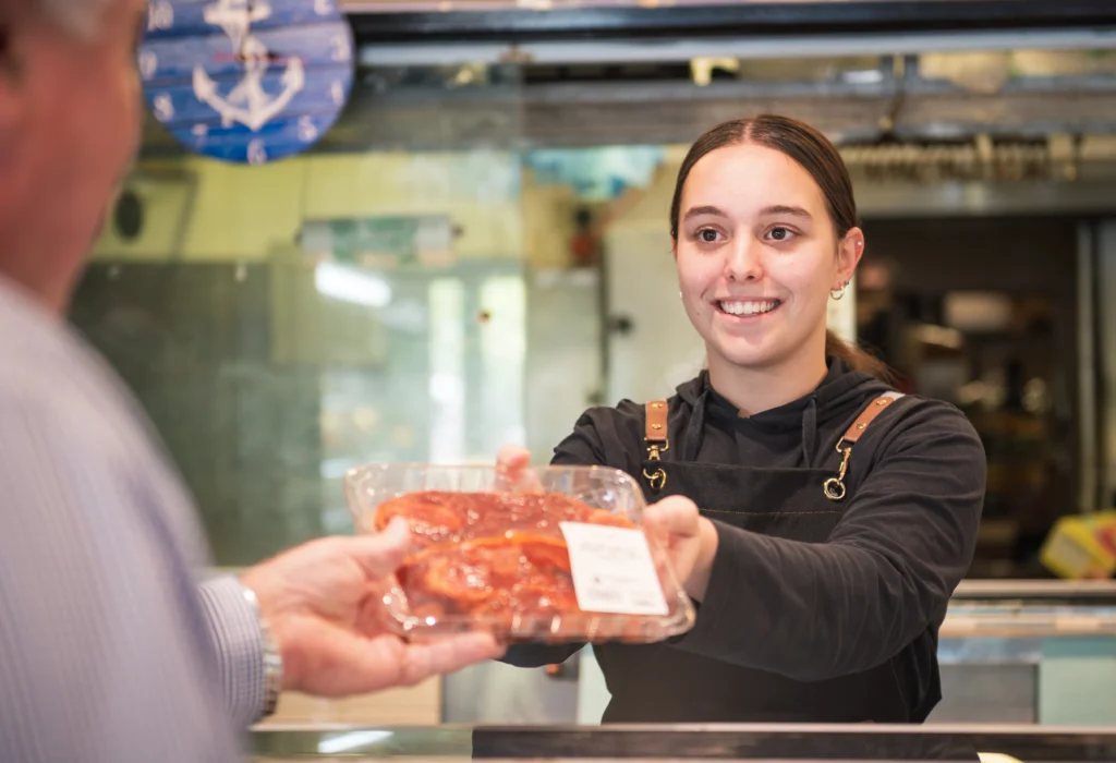 Salesperson at local butcher handing over product to a customer.